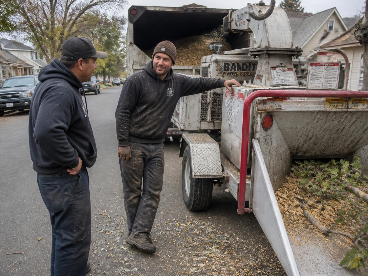 Two local tree service workers talking beside their chipper on a residential street